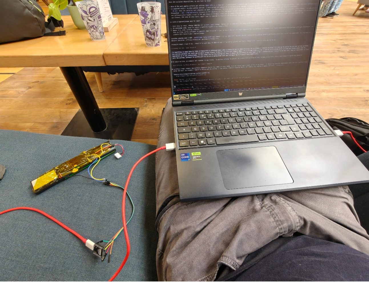Le laboratoire du lendemain : sur un canapé, le pack Neato sous ruban kapton jaune relié par trois fils à un ESP32-C3, lui-même branché en USB à un ordinateur portable dont l'écran affiche les relevés de la jauge