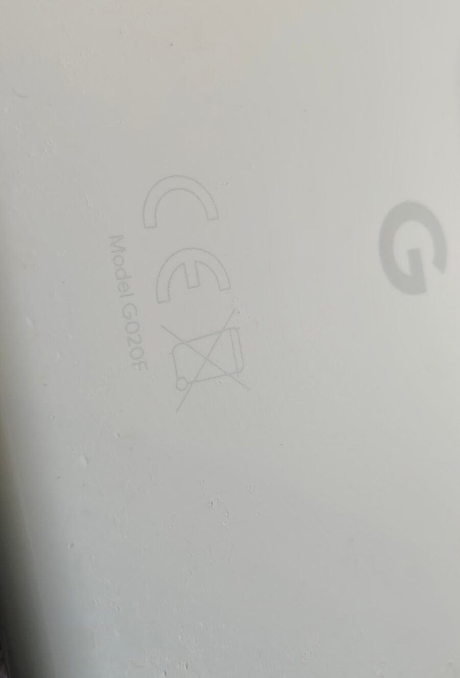 Le dos du Pixel 3a : gravés dans le plastique blanc, le marquage CE, la poubelle sur roues barrée d'une croix, la mention « Model G020F », et le G de Google