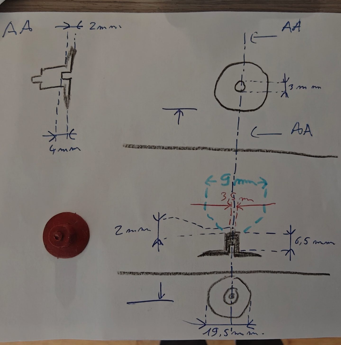 Croquis à main levée d'une ventouse coté au stylo bleu, vue de dessus, coupe A-A et vue de dessous, avec la ventouse rouge posée à côté de la feuille
